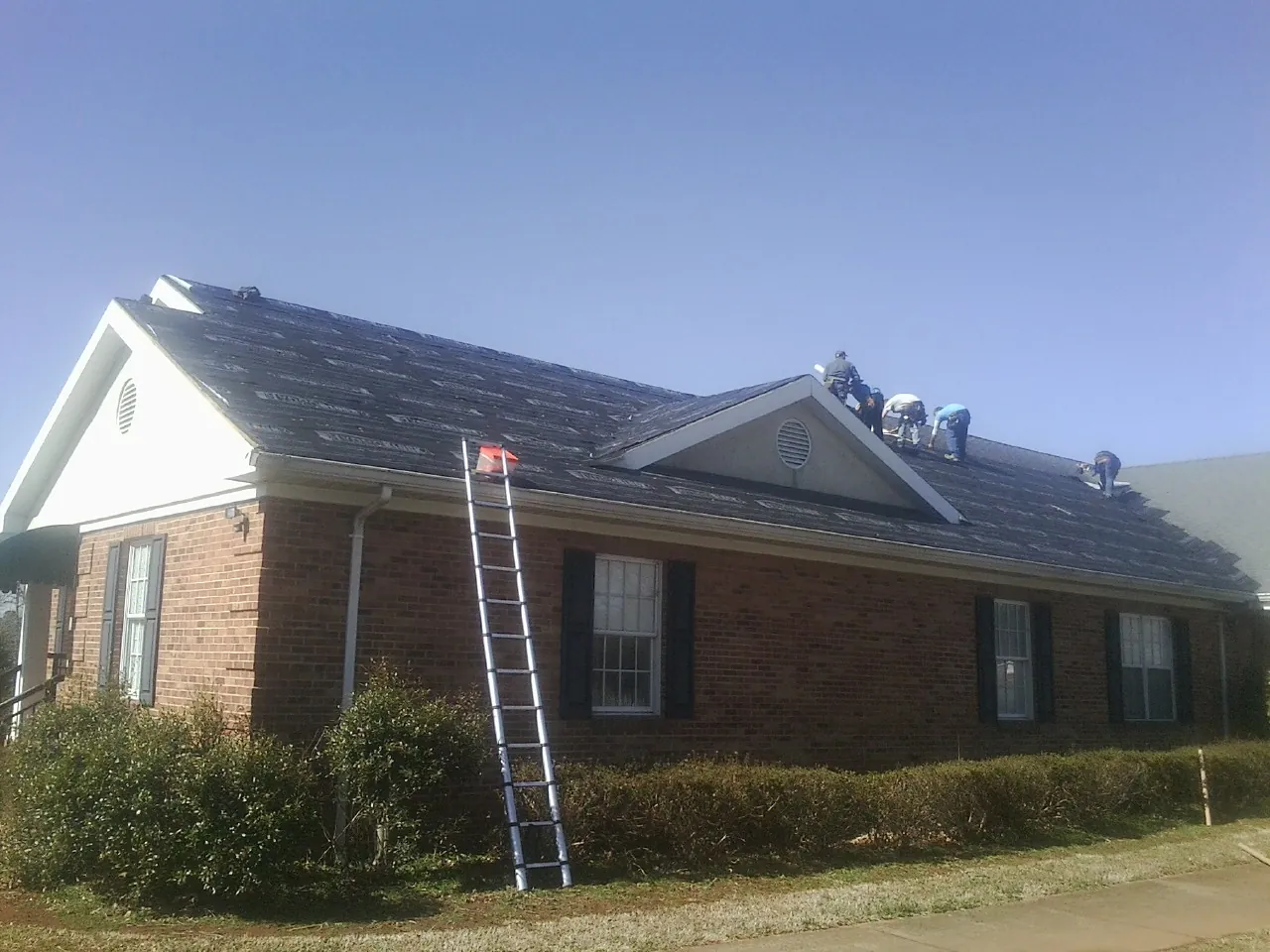 Crew tearing shingles off a brick ranch roof with a ladder set — Emergency Roof Repair work by our crew in Weyauwega