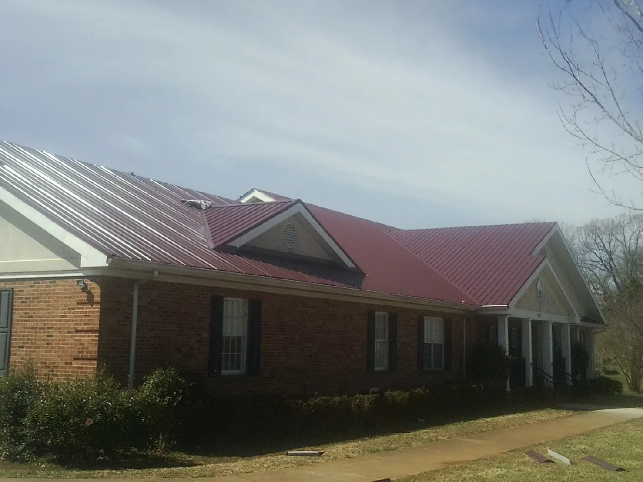 Red metal roof with gabled entries on a long brick building, from a Hail Damage Roof Repair job in Weyauwega