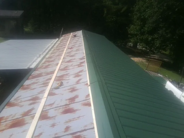 Old rusted panels beside newly installed green metal roofing — Wind Damage Roof Repair by Roofing Brothers in Weyauwega