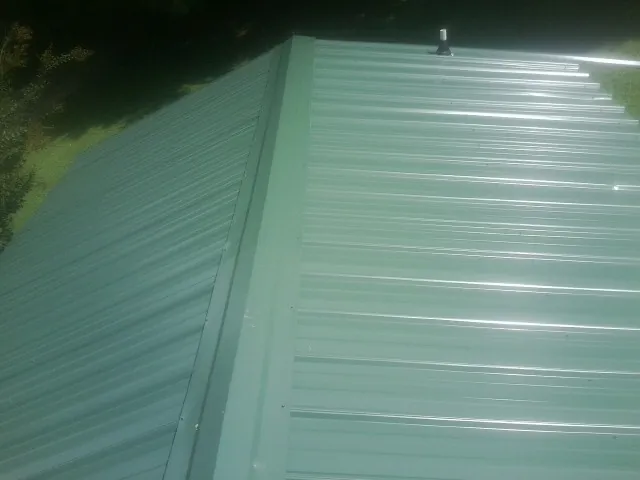 New green metal panels meeting at the ridge of a roof — Flat Roof Repair work by our crew in Weyauwega