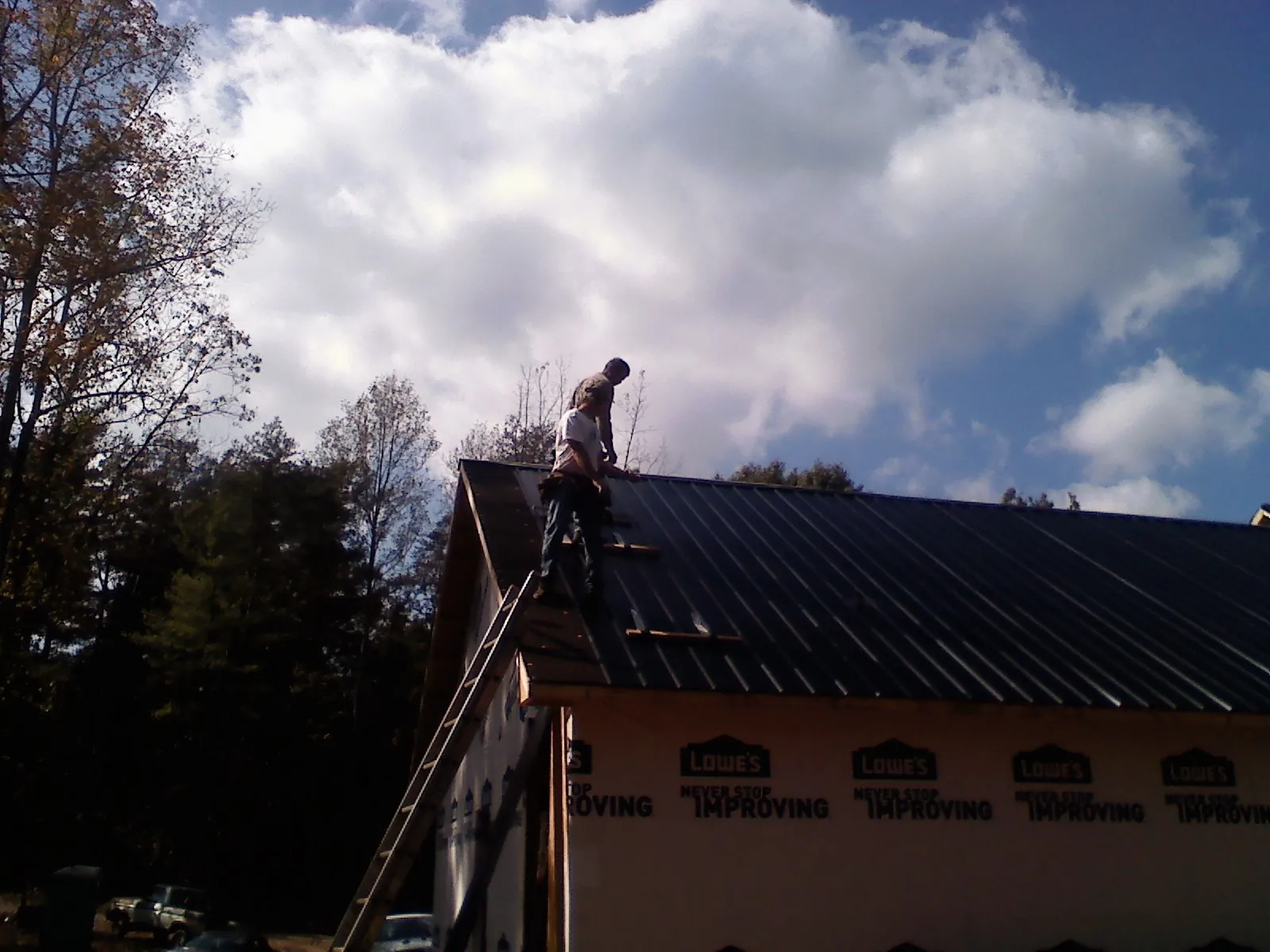 Roofer fastening dark metal panels high against a cloudy sky, from a Roof Inspection job in Weyauwega
