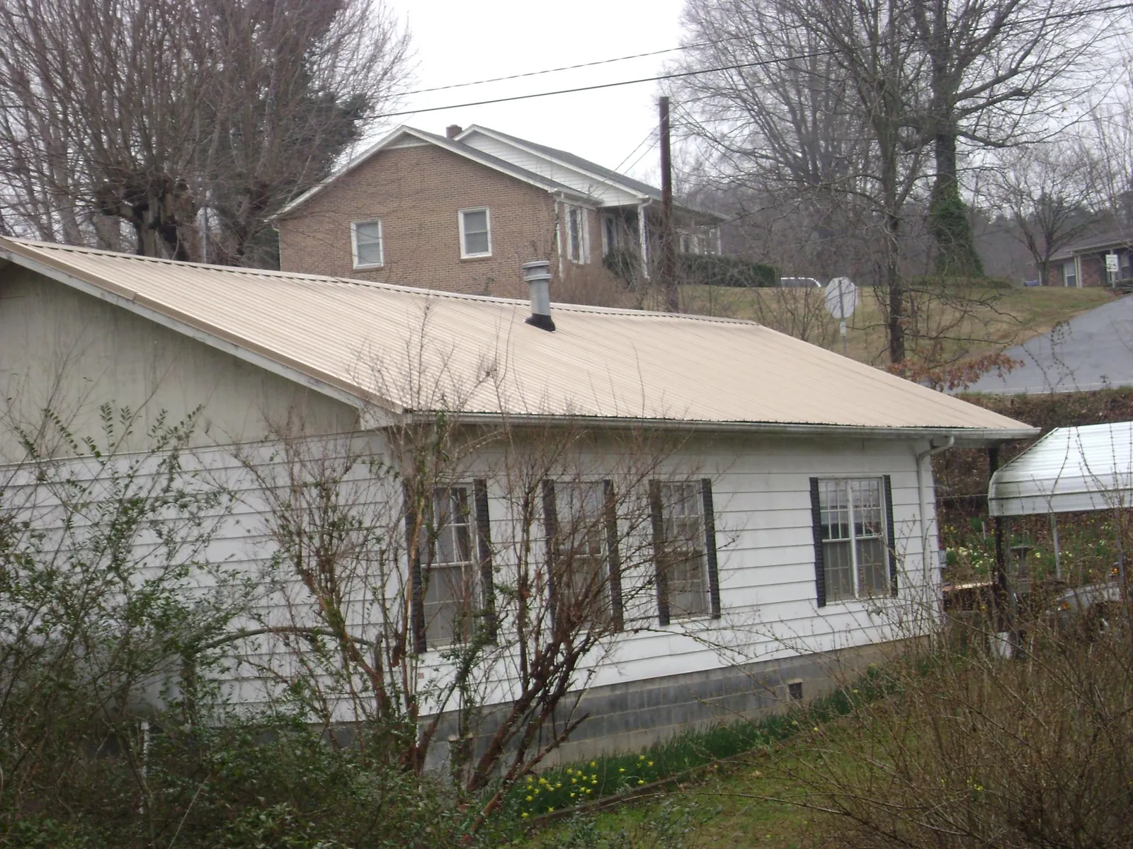 Tan metal roof on a white sided house set into a hillside — Commercial Roofing by Roofing Brothers in Weyauwega
