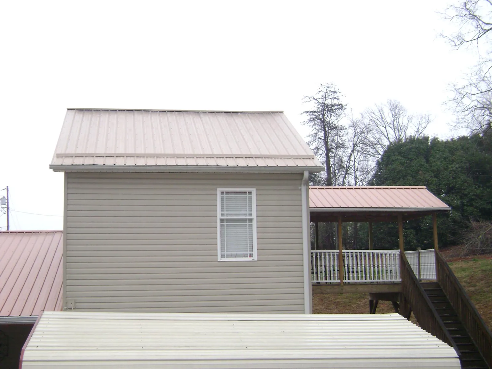 Tan metal roofs on a two story addition and attached porch, from a Roof Replacement job in Weyauwega
